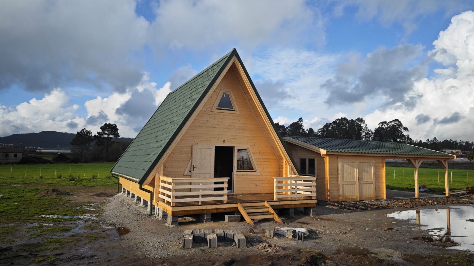 Casa A-Frame concluída com alpendre, guardas em madeira, garagem e telheiro, sob céu azul